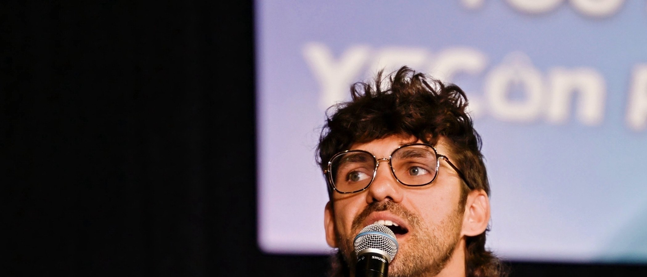 Reef Colman speaking on stage, microphone in hand
