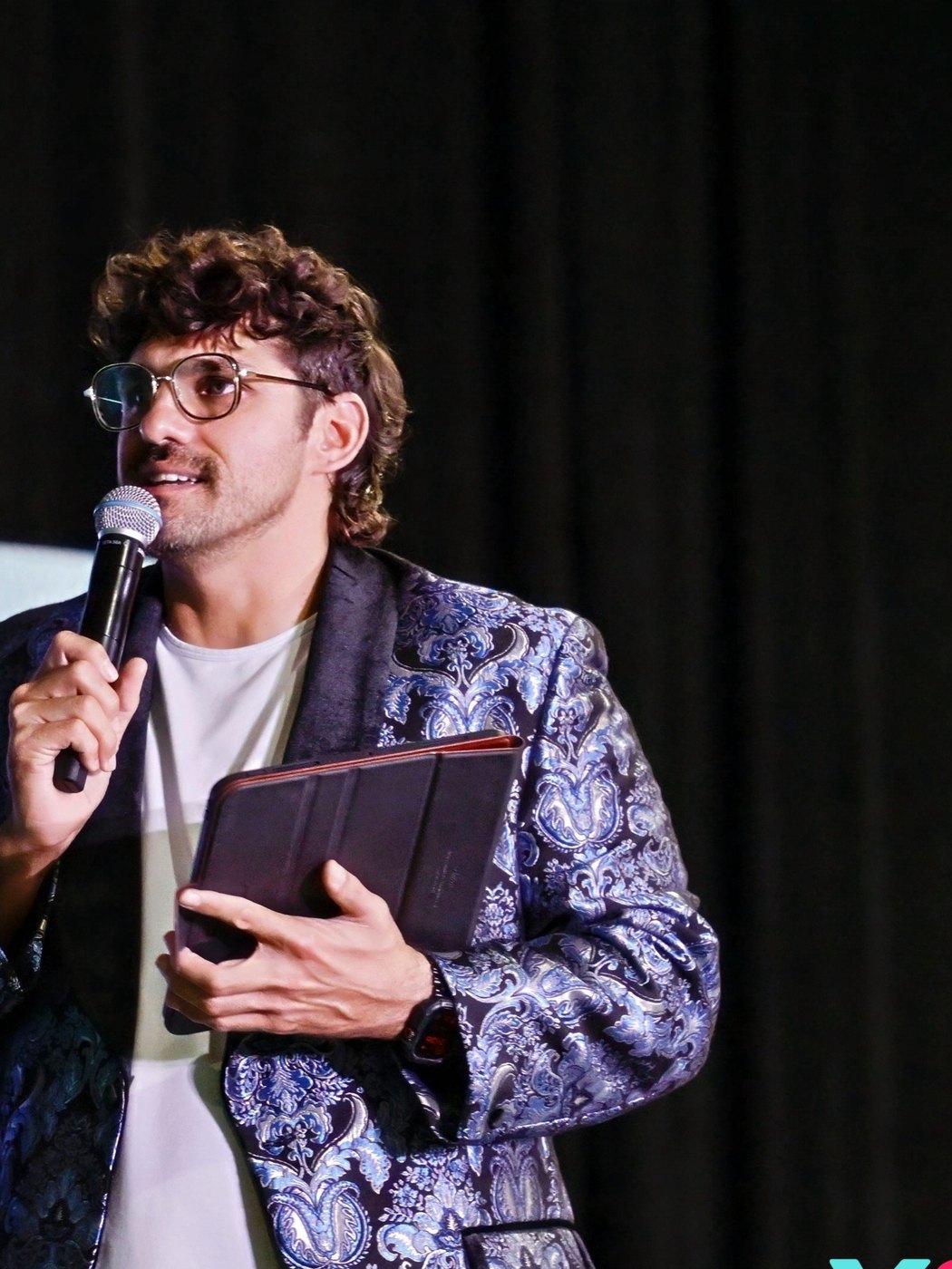 Reef Colman on stage with a microphone and a tablet